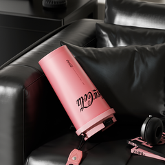 Pink Coca-Cola cup on a black leather couch with headphones and a book.