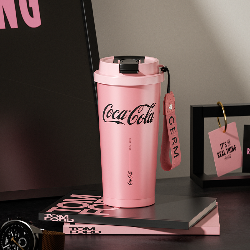 Pink Coca-Cola tumbler with a strap on a dark surface