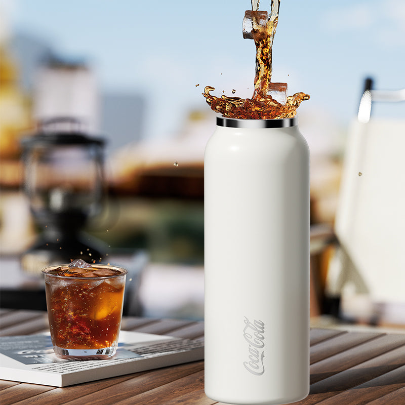 White Coca-Cola bottle with liquid being poured into a glass on a wooden surface.