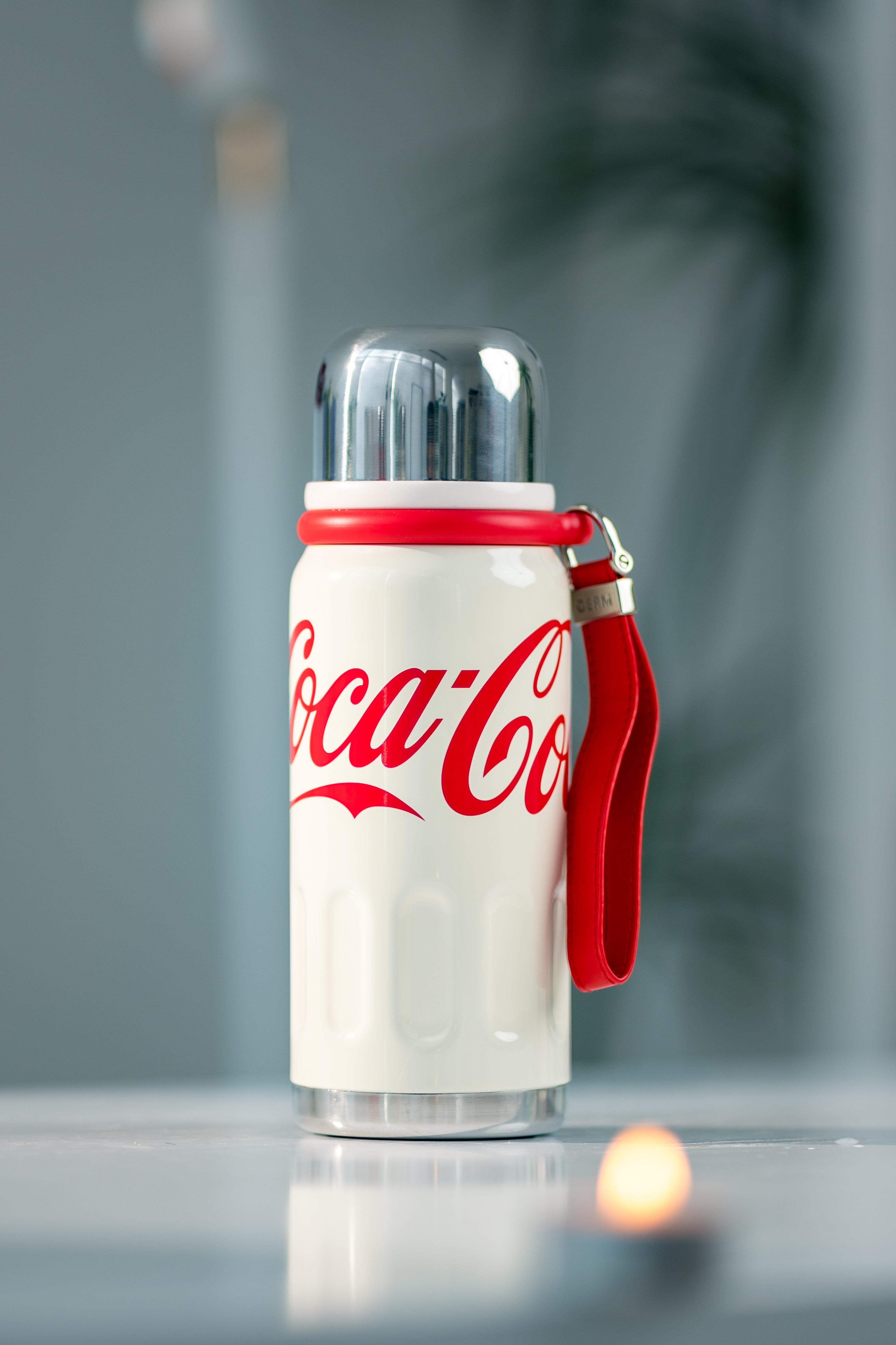 Coca-Cola thermos bottle with red handle on a reflective surface