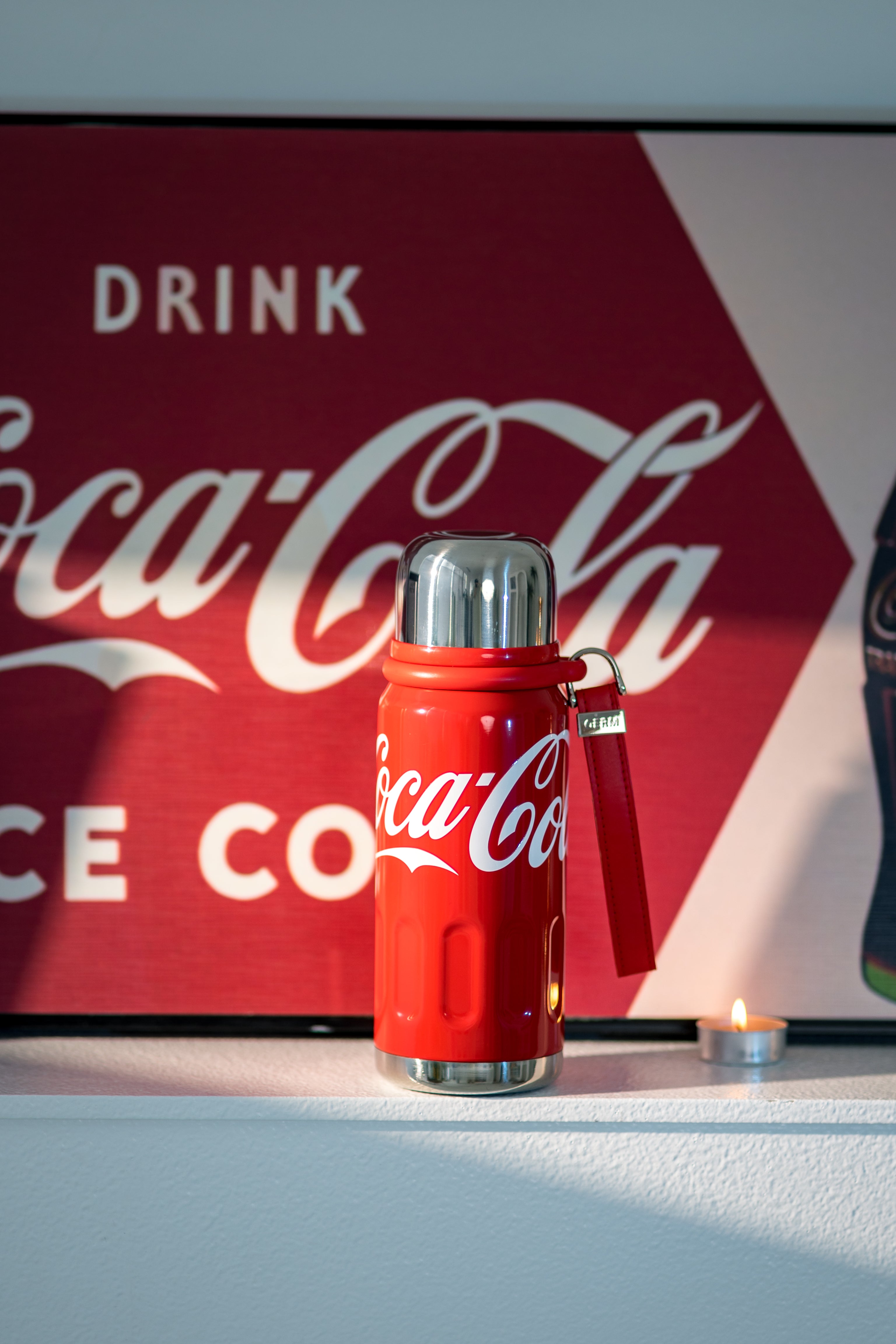 Red Coca-Cola thermos with a vintage sign in the background