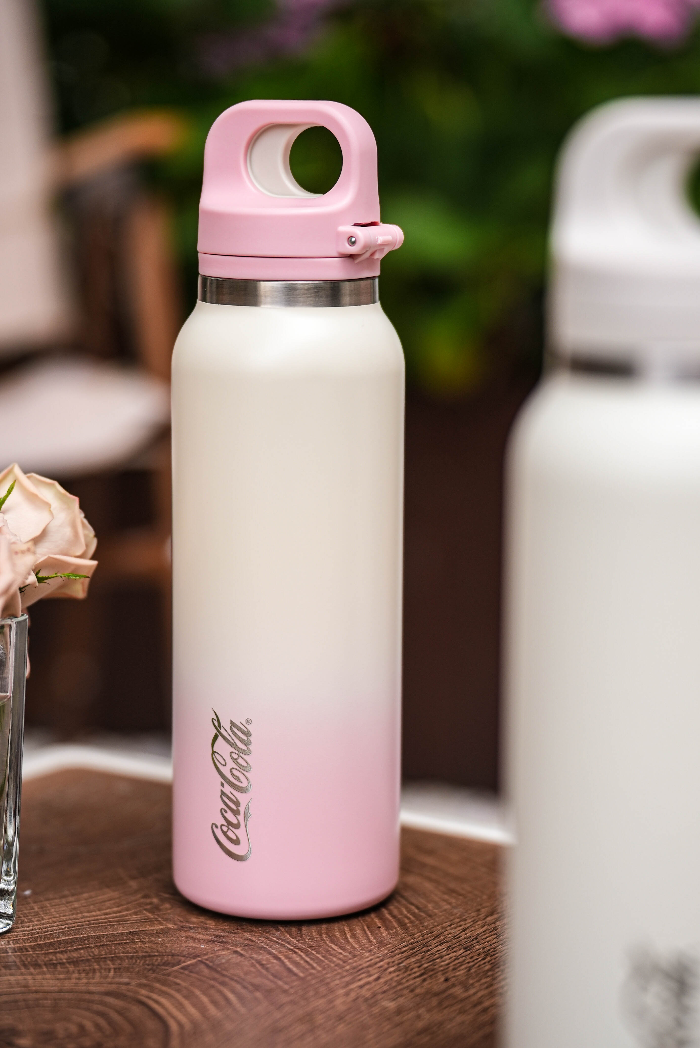 Gradient pink to white Coca-Cola water bottle on a wooden surface with blurred background