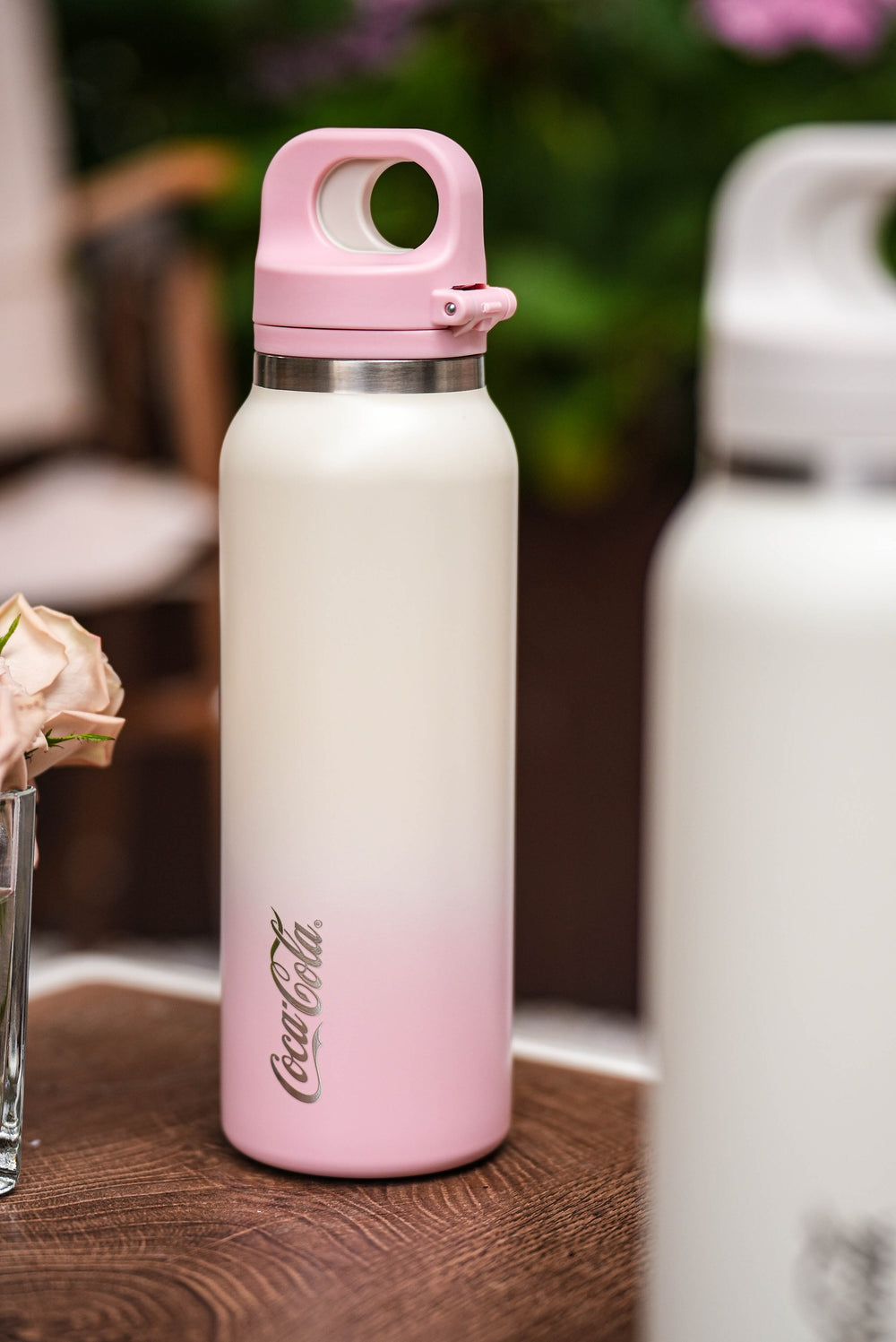 Gradient pink to white Coca-Cola water bottle on a wooden surface with blurred background