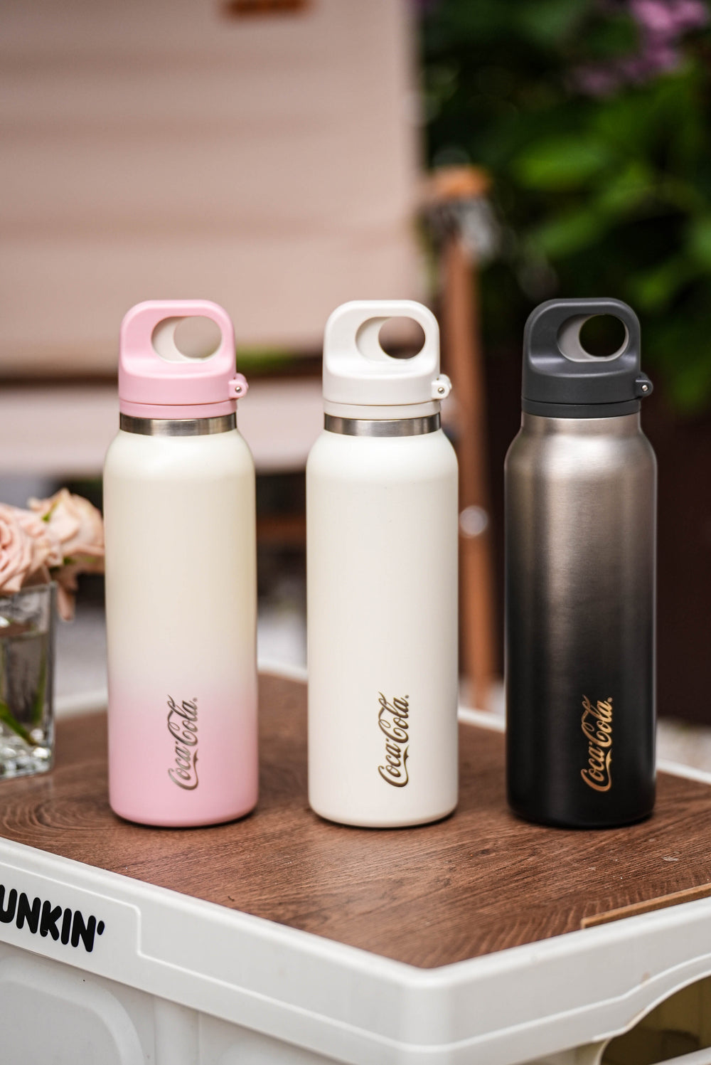 Three Coca-Cola water bottles on a wooden surface with a blurred background