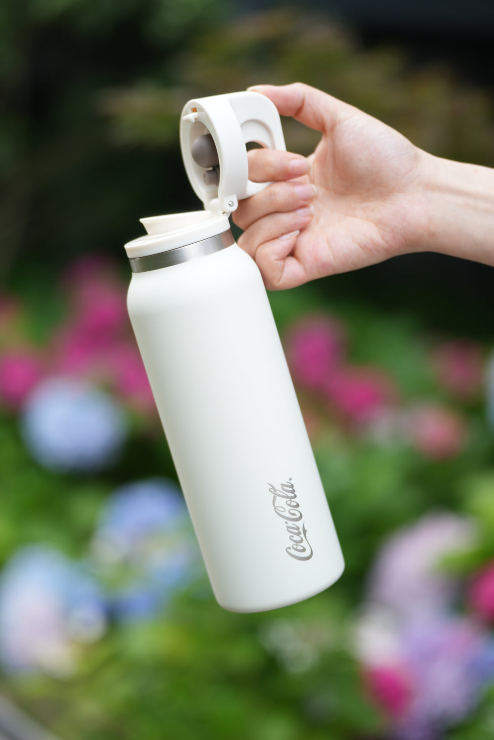 White water bottle held by a hand with a blurred floral background